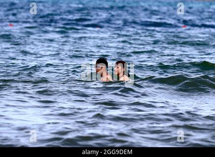 Keelung, Taipei, Taiwan. August 2021. Ein Paar schwimmt im Meer in der Nähe eines Strandes in Keelung, wo die Menschenmenge kontrolliert wird, da Taiwan laut dem taiwanesischen CDC nur 3 lokal erworbene Fälle und null Todesfälle meldet. Nachdem die Versammlungen und Schwimmaktivitäten wieder aufgenommen wurden, verzeichnet die selbstregierte Insel seit ihrem schweren Ausbruch im Mai einen Abwärtstrend bei einheimischen Covid-Infektionen und -Todesfällen, indem sie Impfstoffe für AstraZeneca, Medigen und Moderna zur Verfügung stellt, während sie Impfstoffspenden aus den USA, Japan, Litauen und der Tschechischen Republik erhält. Angesichts der zunehmenden militärischen Bedrohungen Chinas. (Kredit Imag Stockfoto