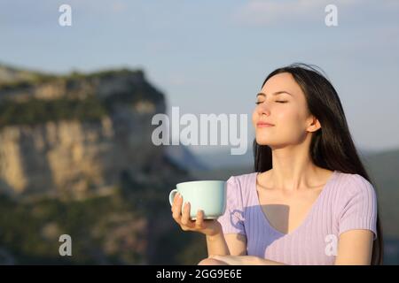 Asiatische Frau, die Kaffee trinkt und bei Sonnenuntergang die Natur genießt Stockfoto