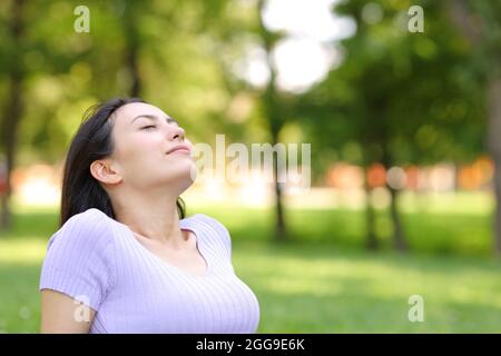 Entspannte asiatische Frau, die frische Luft atmet, sitzt in einem Park Stockfoto