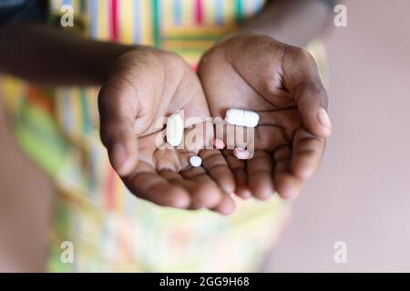 Vielzahl von Pillen und Tabletten in der Handfläche eines unerkennbaren schwarzen Kindes; pharmazeutisches Verräterkonzept Stockfoto