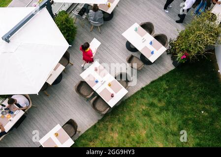 Sommercafe mit Besuchern. Die Arbeit des Kellners auf der Sommerterrasse. Offener Bereich mit Tischen und Stühlen. Blick von oben Stockfoto