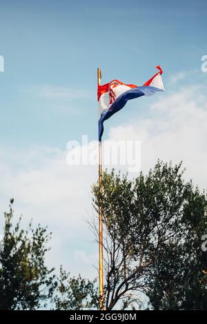 Winken im Wind kroatische Flagge gegen blauen Himmel über Bäumen Stockfoto