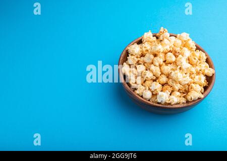 Popcorn mit Karamell in Holzschüssel auf pastellblauem Hintergrund. Seitenansicht, Kopierbereich. Stockfoto