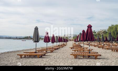 Leere Holzdeckelbetten und gefaltete Sonnenschirme auf Sand in der Nähe der Ägäis. Lounge Chill Zone am Stadtstrand in Athen, Griechenland Stockfoto