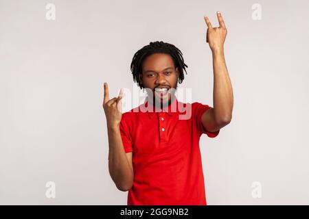Es ist ein Rock'n Roll Baby! Porträt eines bärtigen Mannes mit Dreadlocks in einem roten T-Shirt im lässigen Stil, der mit Rock-Singen und offenem Mund die Kamera anschaut. Indoo Stockfoto