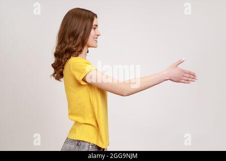 Lassen Sie mich mich mich vorstellen. Profilportrait eines freundlichen, braunhaarigen Teenagers, das Handschlag gab und die Gäste mit einem toothy Lächeln begrüßte. Innen s Stockfoto