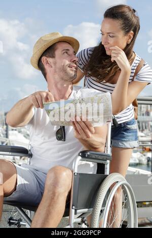 Mann im Rollstuhl im Urlaub mit Frau mit lokalem Stadtplan Stockfoto