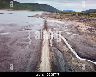 Garve, Schottland, Großbritannien. 30. August 2021.der niedrige Wasserstand im Stausee von Loch Glascarnoch bei Garve hat bisher verborgene Strukturen enthüllt, darunter eine alte Straße, eine Brücke und Telegrafenmasten. Die alte Straße war die Hauptroute von Ullapool nach Dingwall, bis die aktuelle neue Straße neben dem Stausee gebaut wurde. Der Stausee in Glen Glascarnoch wurde in den 1950er Jahren als Teil des Wasserkraftwerks Conon gegründet. Iain Masterton/Alamy Live News. Stockfoto