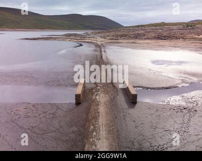 Garve, Schottland, Großbritannien. 30. August 2021.der niedrige Wasserstand im Stausee von Loch Glascarnoch bei Garve hat bisher verborgene Strukturen enthüllt, darunter eine alte Straße, eine Brücke und Telegrafenmasten. Die alte Straße war die Hauptroute von Ullapool nach Dingwall, bis die aktuelle neue Straße neben dem Stausee gebaut wurde. Der Stausee in Glen Glascarnoch wurde in den 1950er Jahren als Teil des Wasserkraftwerks Conon gegründet. Iain Masterton/Alamy Live News. Stockfoto