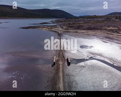 Garve, Schottland, Großbritannien. 30. August 2021.der niedrige Wasserstand im Stausee von Loch Glascarnoch bei Garve hat bisher verborgene Strukturen enthüllt, darunter eine alte Straße, eine Brücke und Telegrafenmasten. Die alte Straße war die Hauptroute von Ullapool nach Dingwall, bis die aktuelle neue Straße neben dem Stausee gebaut wurde. Der Stausee in Glen Glascarnoch wurde in den 1950er Jahren als Teil des Wasserkraftwerks Conon gegründet. Iain Masterton/Alamy Live News. Stockfoto