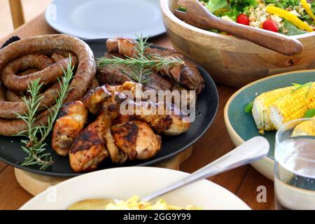 Grillen Sie Fleisch, Huhn und Boerewors auf Teller, fertig zum Essen mit Salat und Mais Stockfoto