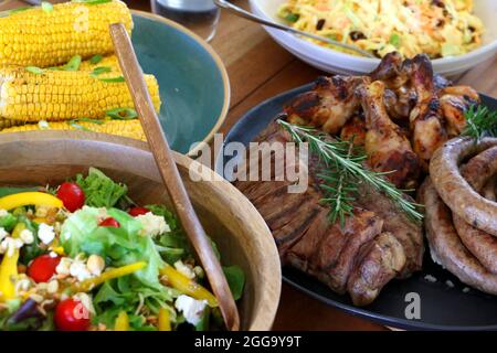 Grillen Sie Fleisch, Huhn und Boerewors auf Teller, fertig zum Essen mit Salat und Mais Stockfoto