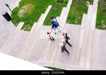 Die Familie läuft im Park. Vater und Mutter halten ihre kleinen Kinder an der Hand. Eltern führen ihre Kinder die Treppe hinauf. Spaß für die ganze Familie und Stockfoto