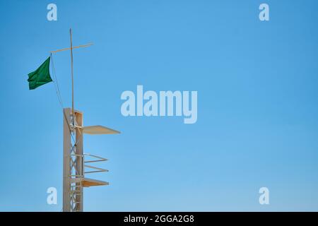 Rettungsschwimmer ohne Rettungsschwimmer und mit grüner Flagge an einem ruhigen Strand mit dem Meer im Hintergrund und einem sonnigen Tag Stockfoto