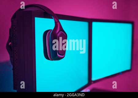 Kabellose Kopfhörer, die am Computerdisplay hängen. Leerer Monitor, um den Inhalt einzufügen. Professionelle Computerspiel spielen, eSport Business und online Stockfoto