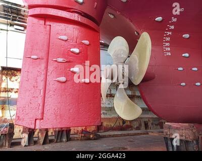 Das Heck eines großen Schiffes mit einem Kupferpropeller, mit einem Lenkgetriebe auf einem Slipway in einem Trockendock. Trockenfrachtschiff im Trockendock für Reparaturen und Wartung Stockfoto