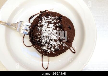 Brownie auf einem weißen Teller Draufsicht. Schokoladenbrownie mit Schokoladensauce und Puderzucker auf einem weißen Teller. Dessert auf einem Teller in einem Café. Draufsicht. Stockfoto