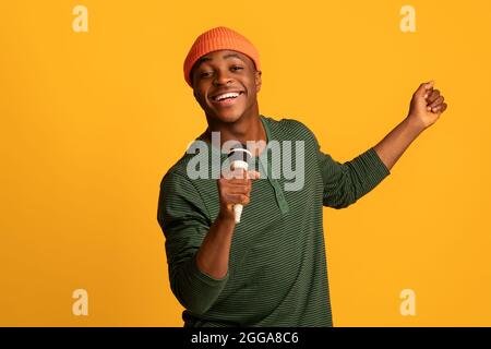 Fröhlicher Black Millennial Guy Hält Mikrofon Und Singt Bei Der Kamera Stockfoto