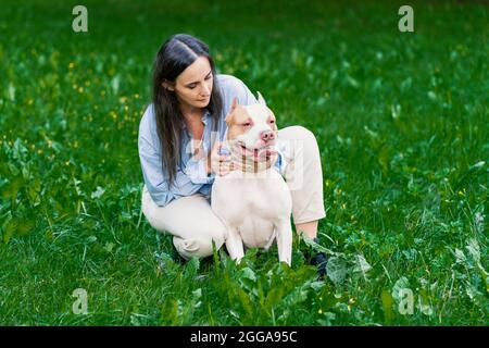 Frau in casual streicheln amerikanischen Pitbull Terrier auf Gras. Glücklicher Hund mit der Zunge, der sich umsieht Stockfoto