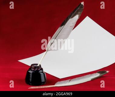 Zwei Federkiel-Stifte mit einem Blatt Schreibpapier und einer Tintenflasche auf rotem Hintergrund Stockfoto