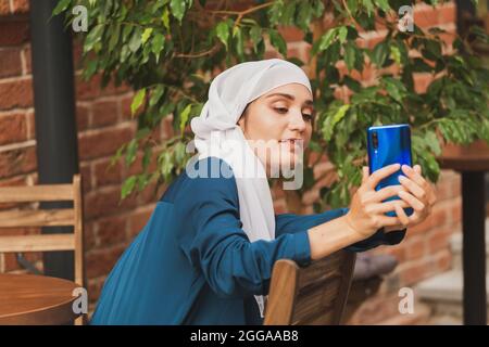 Muslimische Frau nimmt Selfie. Glücklich schönes Mädchen mit Schal nehmen Sie ein Bild von sich selbst mit dem Smartphone. Stockfoto