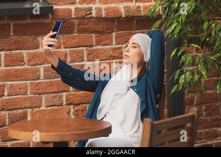 Muslimische Frau nimmt Selfie. Glücklich schönes Mädchen mit Schal nehmen Sie ein Bild von sich selbst mit dem Smartphone. Stockfoto