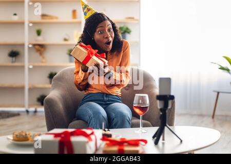 Überrascht African American Lady Holding Geschenk Feiert Geburtstag Online Indoor Stockfoto