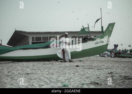 Pakistanische Fischer stehen neben einem traditionellen Fischerboot am Strand. Stockfoto