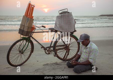 Mann, der Eis am Strand verkauft, bei Sonnenuntergang mit seinem Fahrrad. Stockfoto