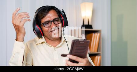 Fröhlicher Geschäftsmann, der im Büro Musik über Kopfhörer hört – Konzept der Pause, Entspannung während der Arbeit Stockfoto
