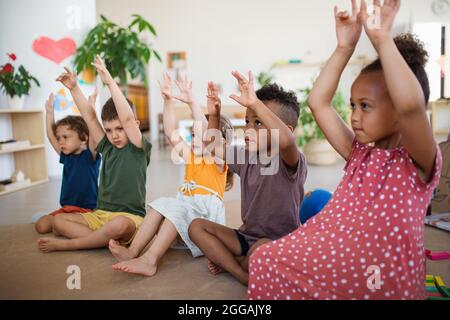 Gruppe von kleinen Kindergartenkindern, die im Klassenzimmer auf dem Boden sitzen und spielen. Stockfoto
