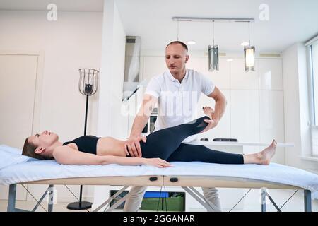 Gutaussehende Physiotherapeutin, die mit einer Patientin in der Arztpraxis arbeitet Stockfoto