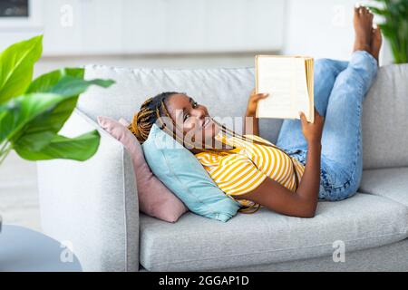 Sorglose schwarze Frau, die auf der Couch liegt und Buch liest Stockfoto