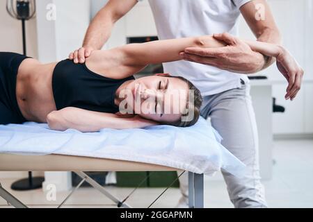 Nicht anerkannte Physiotherapeutin, die mit jungen attraktiven Frauen in der Rehabilitationsklinik arbeitet Stockfoto