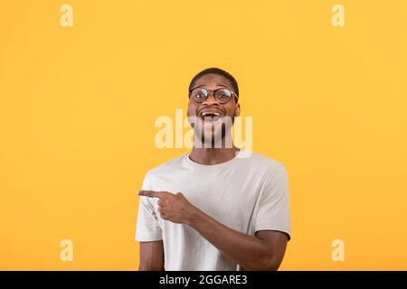 Überrascht afroamerikanischer Mann, der auf den leeren Raum zeigt und die Kamera über dem gelben Studiohintergrund anschaut Stockfoto