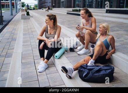 Gruppe von jungen und alten Frauen, die nach dem Training draußen in der Stadt sitzen und sich unterhalten. Stockfoto