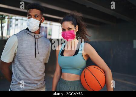 Mann und Frau, die mit Basketball befreundet sind, trainieren in der Stadt draußen und schauen auf die Kamera. Coronavirus-Konzept. Stockfoto