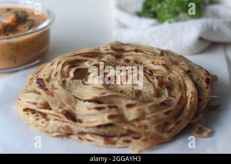 Parotta oder Porotta, ein geschichtetes Fladenbrot aus Maida. Dieser flockige Bändchenpfannkuchen ist ein Favorit von Kerala. Shot mit Butter Hähnchen aus gegrilltem Lch Stockfoto