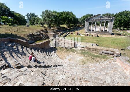 Mutter und Sohn erkunden antike griechische archäologische Ausgrabungen von Apollonia, sitzen im Theater vor den Tempelruinen von Agonothetes, Albanien Stockfoto