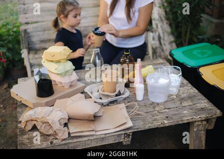 Die junge Mutter mit ihrer kleinen Tochter bereitet sich darauf vor, verschiedene Arten von Müll zu recyceln und in spezielle Behälter zu stecken. Verschiedene Farben von Stockfoto