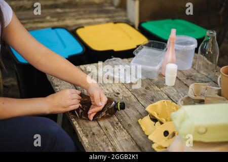 Nahaufnahme einer Frau, die Müll für das Recycling vorbereitet, drückt eine leere Flasche. Frau, die sich um die Natur kümmert. Verschiedene Farben des Behälters Stockfoto