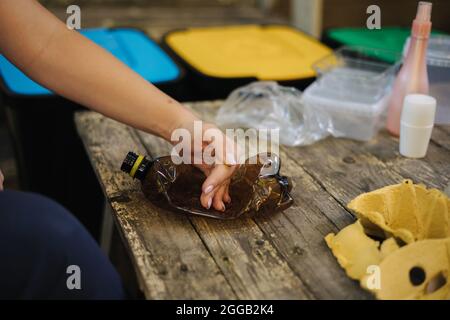 Nahaufnahme einer Frau, die Müll für das Recycling vorbereitet, drückt eine leere Flasche. Frau, die sich um die Natur kümmert. Verschiedene Farben des Behälters Stockfoto