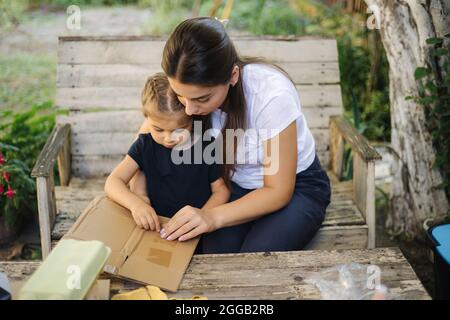 Familie sortiert Müll zu Hause auf dem Hinterhof. Konzept des Recyclings im Freien. Mutter und Tochter kümmern sich um die Natur Stockfoto