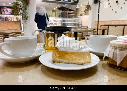 Nahaufnahme eines Stückes transparenter Gelatinekuchen mit Baiser-Creme auf dem Tisch im Café mit verschwommenem Besucher. Stockfoto