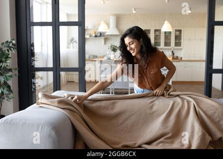 Junge kaukasische Dame, die warmes Karo auf ein bequemes Sofa legt, sich zu Hause auf die Herbst- oder Wintersaison vorbereitet, Platz kopieren Stockfoto