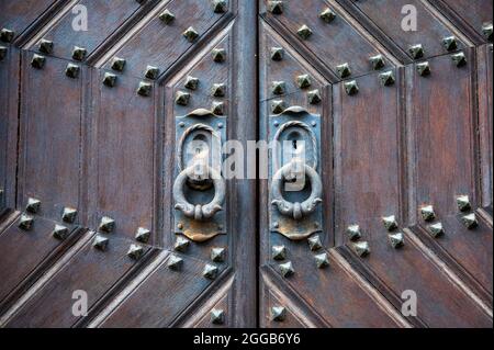 Historische Holztür mit verwitterten Metallbeschlägen und antiken Türklopfern Stockfoto