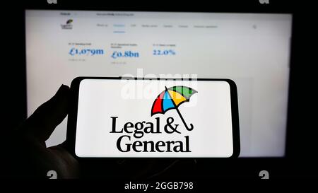 Person mit Mobiltelefon und Logo des britischen Finanzunternehmens Legal General Group plc auf dem Bildschirm vor der Webseite. Konzentrieren Sie sich auf die Telefonanzeige. Stockfoto