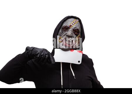 Ein Mann, der in einem schwarzen Kapuzenpullover gekleidet und in einer Zombie-Maske verkleidet ist, hat ein blutiges Schlachtermesser an seinen Hals gedrückt. Der Hintergrund ist weiß Stockfoto