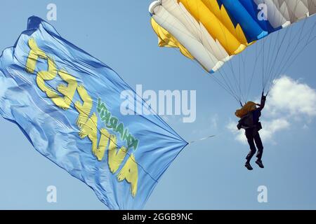 REGION KHARKIV, UKRAINE - 28. AUGUST 2021 - EIN Fallschirmspringer trägt das Banner mit dem Logo der Flugschau KharkivAviaFest 2021 auf dem Flugplatz Korotych Stockfoto