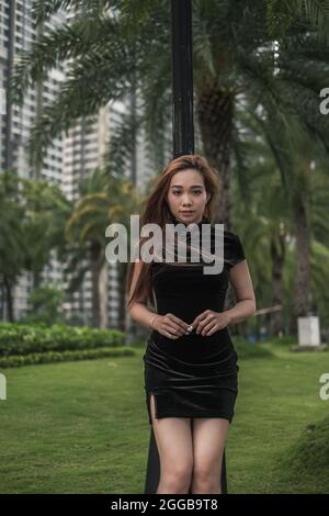 Porträt einer schönen jungen asiatischen Frau in lässigem schwarzen Kleid, die im Park steht. Langes Haar. Schöne Haltung. Reizende Vietnamesin. Stockfoto